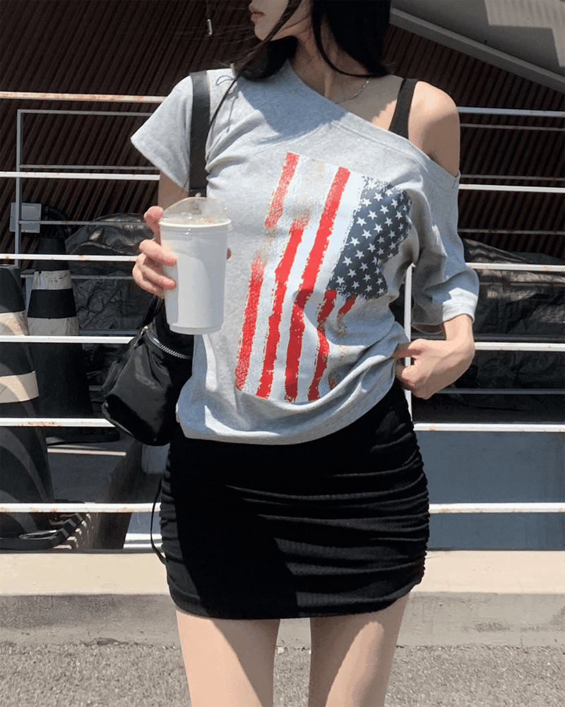 GUSTA（グスタ）の「Beats Unbalanced Off-Shoulder Loose Stars and Stripes Short Sleeve Tee (2 Colors)（Tops）」